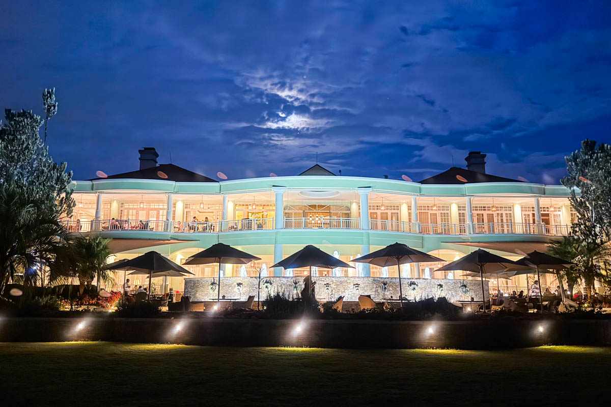A brightly lit two-story building with balconies and outdoor seating, photographed at night under a cloudy, moonlit sky.